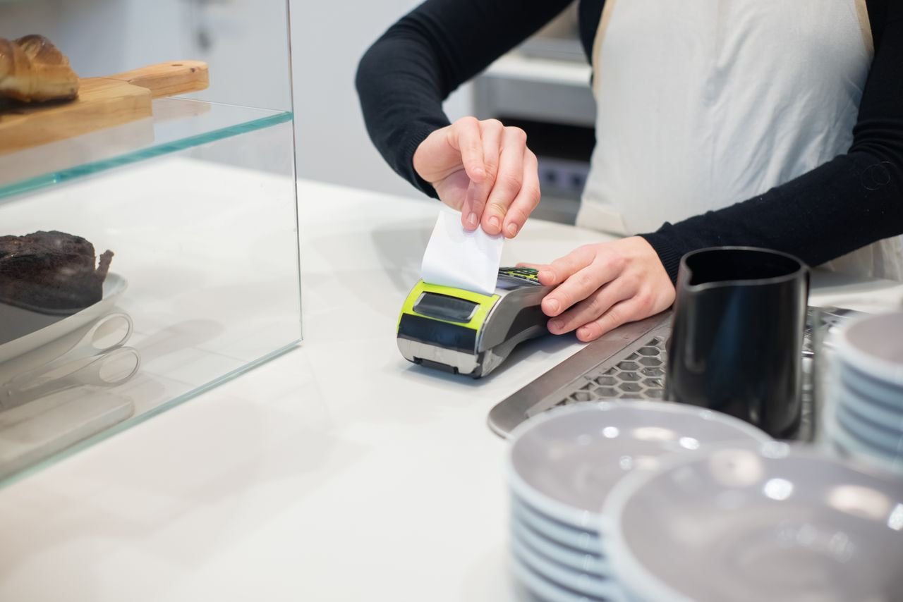 Home Close-up of a cashless transaction at a modern café counter with hands holding a receipt.