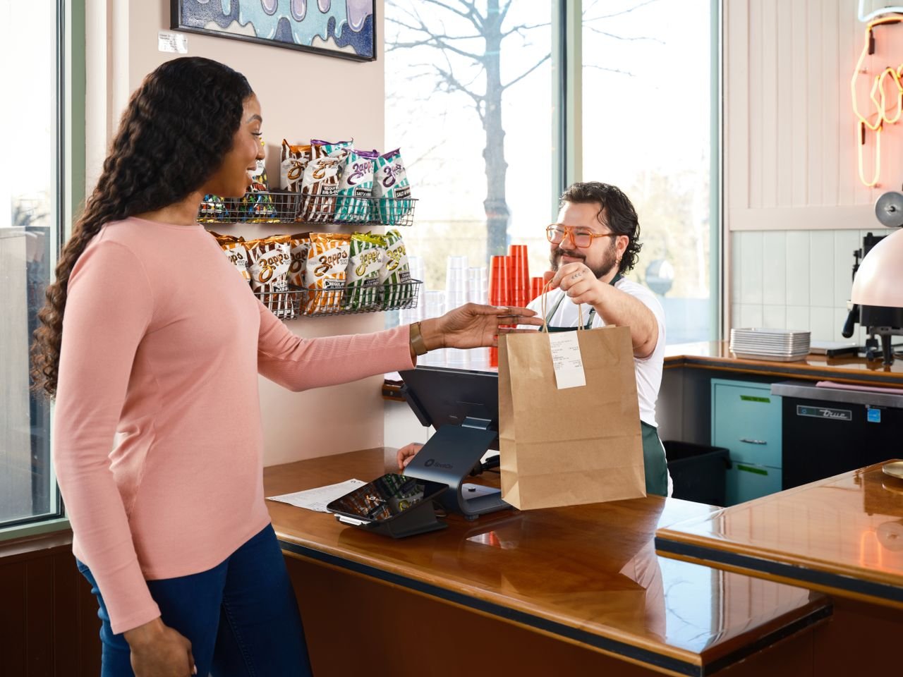 A customer receives a takeout order at a cafe counter, showcasing modern point of sale technology.